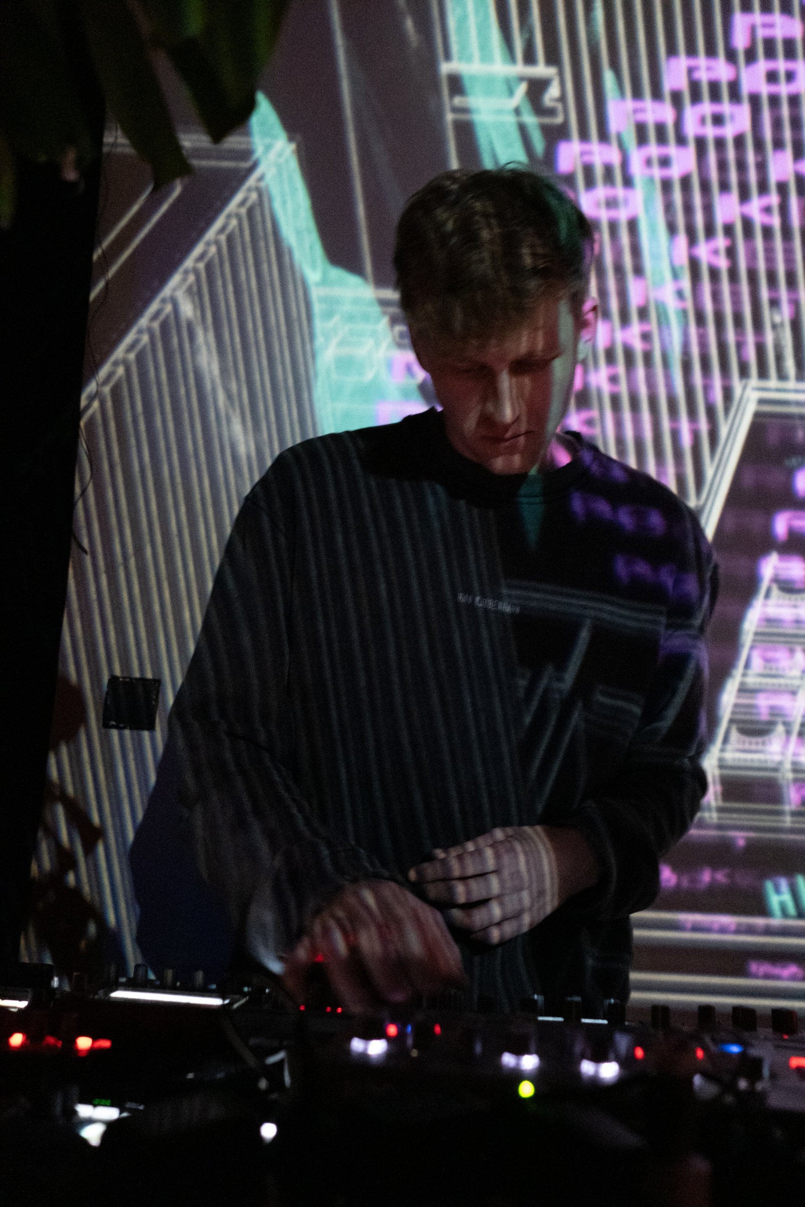 Pocket Rave performing live behind a hardware setup, projected visuals behind him