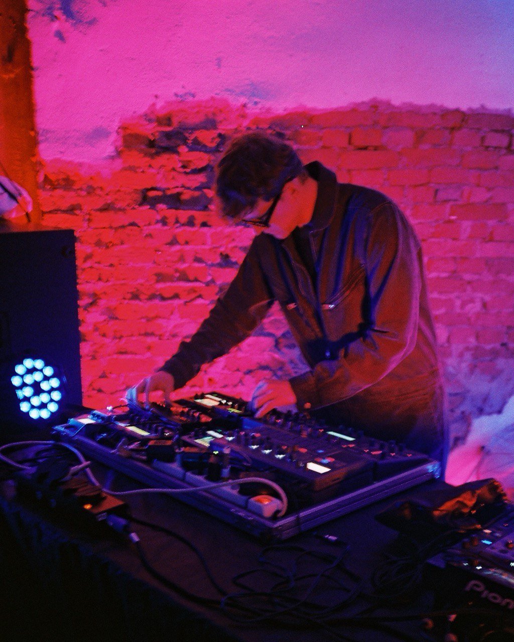 Pocket Rave playing synthesizers against a pink brick wall